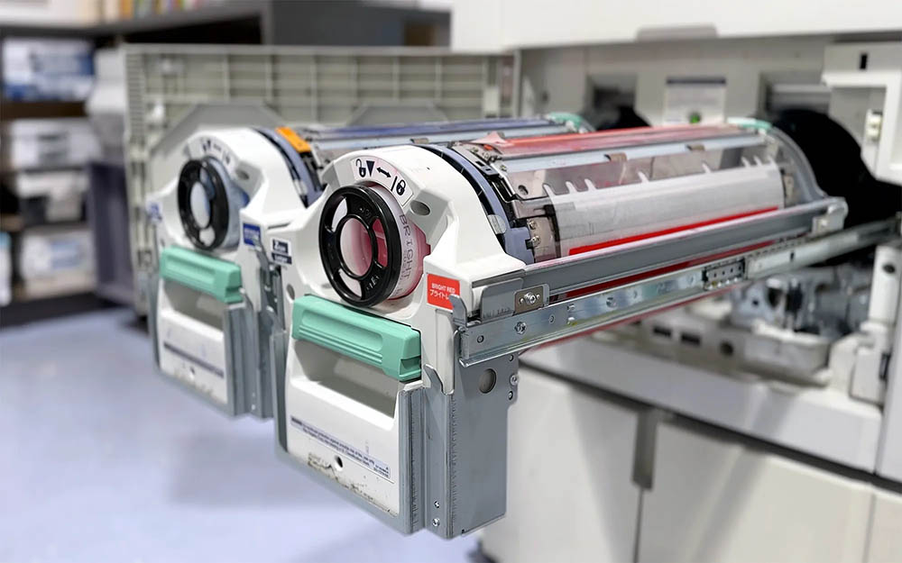 Печать на ризографе в Украине становится всё более востребованной благодаря своей невероятной эффективности, экономичности и простоте использования. Ризограф — это специализированное печатное устройство, которое сочетает в себе черты офсетной печати и копировальной техники, используя трафаретный метод переноса изображения. Такая технология позволяет создавать большие тиражи полиграфической продукции при минимальных затратах времени и материалов, обеспечивая высокую производительность и низкую себестоимость одного оттиска. Процесс печати на ризографе начинается с подготовки оригинал-макета. На этом этапе создаётся изображение, текст или графика, которые будут перенесены на бумагу. Оригинал можно отсканировать, набрать в графическом редакторе или распечатать, после чего он используется для создания трафарета. Внутри ризографа оригинал обрабатывается термочувствительной плёнкой, на которой под воздействием тепла выгорают участки изображения — это и есть будущий трафарет. Трафарет затем наматывается на барабан, внутри которого находится специальная маслянистая краска. При вращении барабана краска под давлением продавливается сквозь отверстия трафарета и переносится на бумагу. Этот процесс очень быстрый и практически не требует вмешательства оператора. Чем больше тираж, тем ниже стоимость одного отпечатка, что делает ризограф особенно выгодным для печати больших партий: листовок, бюллетеней, учебных пособий, методичек, анкет, объявлений, инструкций, бланков и другой массовой печатной продукции. После печати важно дать краске высохнуть — чаще всего это делается естественным путём, но при необходимости можно использовать сушильные устройства для ускорения процесса. Готовые отпечатки сортируются, упаковываются и при необходимости поддаются послепечатной обработке — обрезке, брошюровке, скреплению и т. д. Одним из ключевых преимуществ ризографа является возможность печати на различных типах бумаги, включая офисную, крафтовую, дизайнерскую и переработанную. Это расширяет сферу его применения и позволяет работать даже с нестандартными проектами. Ризографы особенно ценятся в учебных заведениях, копи-центрах, органах местного самоуправления, религиозных организациях, НПО, школах, библиотеках, студиях и малых типографиях. Благодаря простоте использования, невысокому энергопотреблению, доступным расходным материалам и надёжности, ризографы остаются незаменимым инструментом для быстрого и экономичного тиражирования. Если вы ищете способ печати, который сочетает в себе скорость, качество и минимальные затраты — ризограф станет отличным выбором.